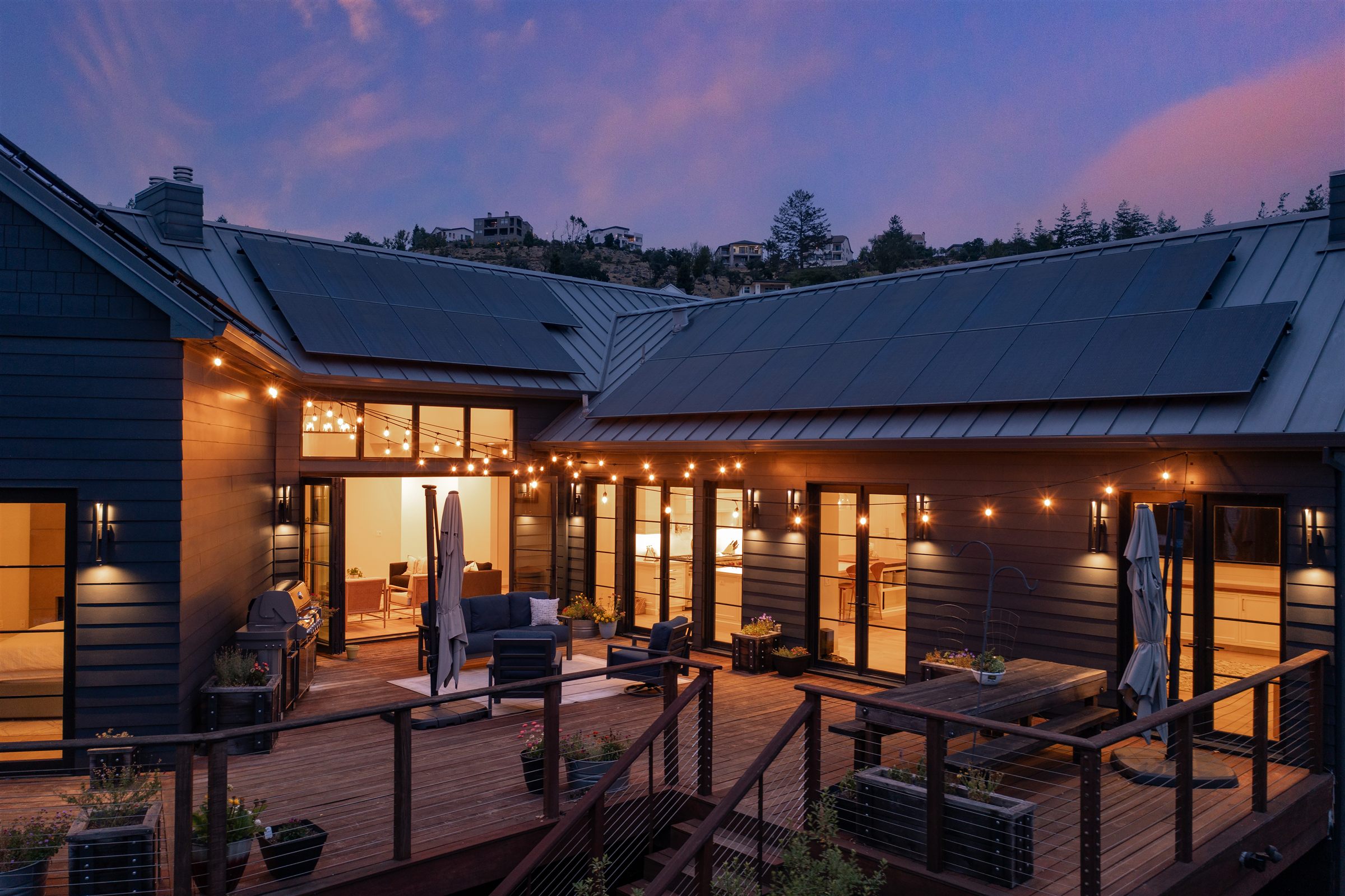 Dusk exterior with string-lit deck and metal roof